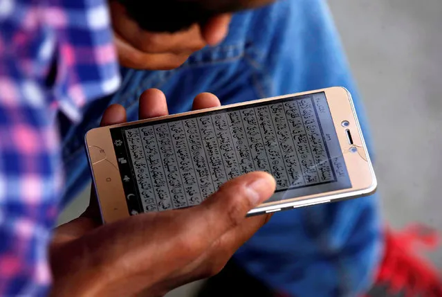 A man reads the Koran on his mobile phone outside a mosque during the holy fasting month of Ramadan, in Srinagar June 14, 2017. (Photo by Danish Ismail/Reuters)