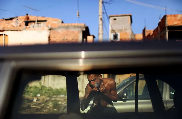 A resident shaves using a car window as a mirror amongst cars parked by World Cup tourists for a fee in the Metro Mangueira favela, located 750 meters from Maracana stadium, where Ecuador and France played today, on June 25, 2014 in Rio de Janeiro, Brazil. Tourists were parking in an area where homes once stood. (Photo by Mario Tama/Getty Images)