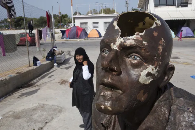 An Afghan woman stands behind the broken head of a statue at the west terminal of an abandoned old airport which is used as a shelter for over 3,500 migrants, in southern Athens, on Monday, May 30 ,2016. The government has been moving migrants from makeshift camps into organized shelters and the Greek government said Monday they will continue to clear the Greek- Macedonian border area over the next few days. (Photo by Petros Giannakouris/AP Photo)