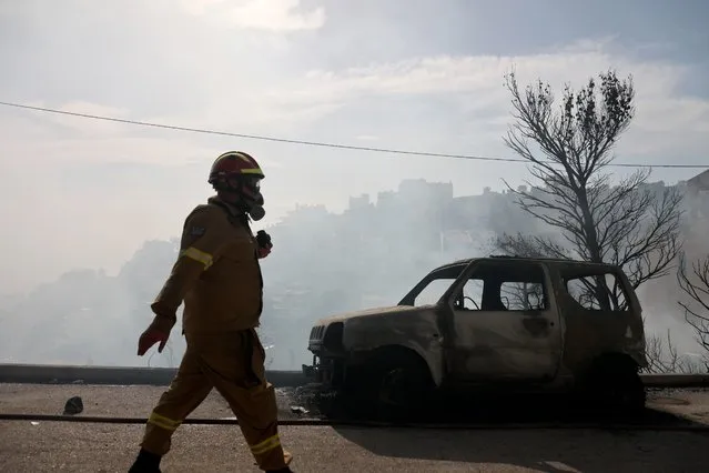 A firefighter walks next to a burnt car during a wildfire in Voula suburb, in southern Athens, Greece, Saturday, June 4, 2022. A combination of hot, dry weather and strong winds makes Greece vulnerable to wildfire outbreaks every summer. (Photo by Yorgos Karahalis/AP Photo)