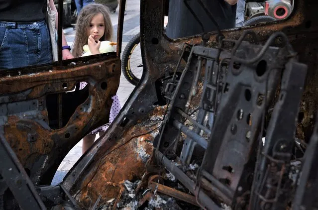 A child looks at a destroyed vehicle in Kyiv on June 13, 2022. War and innocence collide as people view an exhibit in Michailovskyi Square. A child's innocence clothed in a frilly dress is framed by a scorched car, little boys play soldier, a woman strikes a pose atop a tank for her date to make snapshots. Life goes on in Kyiv as war rages in the east. Curiosity is strong as people need to look at the hardware causing so much destruction in their land. (Photo by Carol Guzy/ZUMA Press Wire/Rex Features/Shutterstock)