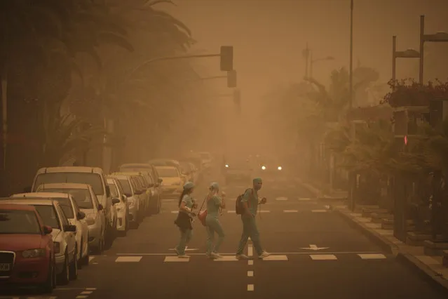 People in carnival dress walk across a street crossing in a cloud of red dust in Santa Cruz de Tenerife, Spain, Sunday, February 23, 2020. Flights leaving Tenerife have been affected after storms of red sand from Africa's Saharan desert hit the Canary Islands and carnival was finally cancelled it was announced. (Photo by Andres Gutierrez/AP Photo)