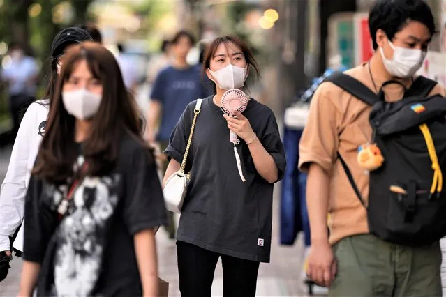 A woman uses a portable electric fan while strolling down the street with her friends in Tokyo, Monday, June 27, 2022. The Japanese government warned of possible power shortages Monday in the Tokyo region, asking people to conserve energy as the country endures an unusually intense heat wave. (Photo by Hiro Komae/AP Photo)
