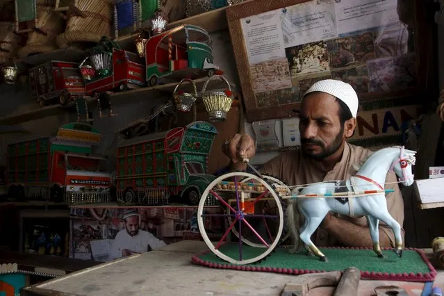 Artisan, Niaz Ali, works on a figurine of a horse pulling a cart at his decorative toy shop in Peshawar, Pakistan, August 13, 2015. (Photo by Khuram Parvez/Reuters)
