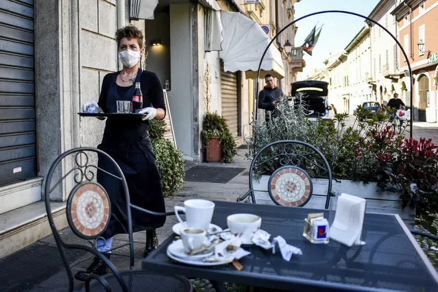 A waitress wears a mask and gloves as she carries a tray at a cafe in the town of Codogno, in the region of Lombardia, northern Italy, Wednesday, March 11, 2020. The Lombardy cluster of COVID-19 was first registered in the tiny town of Codogno on Feb. 19, when the first patient tested positive and has been a red zone until the end of seclusion and return of production in the recent days. For most people, the new coronavirus causes only mild or moderate symptoms, such as fever and cough. For some, especially older adults and people with existing health problems, it can cause more severe illness, including pneumonia. (Photo by Claudio Furlan/LaPresse via AP Photo)