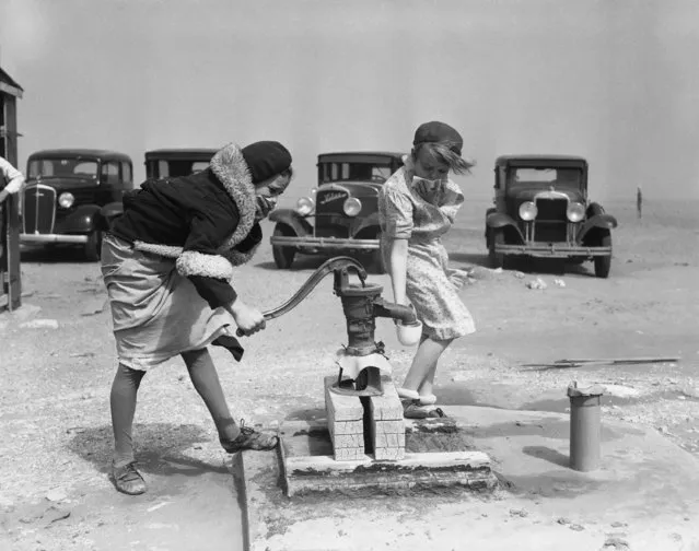 In this March 25, 1935 file photo, children cover their faces during a swirling dust storm while pumping water in Springfield, Colo. The Dust Bowl was manmade, born of bad farming techniques across millions of acres in parts of Texas, Oklahoma, New Mexico, Colorado and Kansas. Now, even as bad as the drought is in some of those same states, soil conservation practices developed in the aftermath of the Dust Bowl have kept the nightmarish storms from recurring. (Photo by AP Photo)