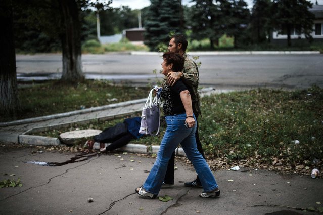 A man comforts his mother as they walk past the body of man lying on the pavement after shelling in the town of Makiyivka on August 19, 2014. Ukraine said Tuesday that fighting had erupted in the heart of the major rebel stronghold of Lugansk as government forces pressed on with a punishing offensive to win back the war-torn east. (Photo by Dimitar Dilkoff/AFP Photo)