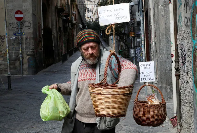 A man takes products from a basket, that were hung up so people can donate or take for free food, as Italy struggles to contain the spread of coronavirus disease (COVID-19), in Naples, Italy on March 30, 2020. The sign reads: “Who can puts in, who can't takes”. (Photo by Ciro De Luca/Reuters)