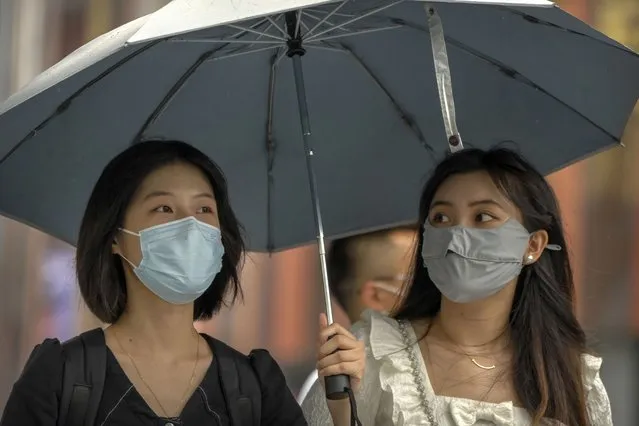 Women wearing face masks walk under an umbrella at a shopping complex in Beijing, Saturday, August 6, 2022. (Photo by Mark Schiefelbein/AP Photo)
