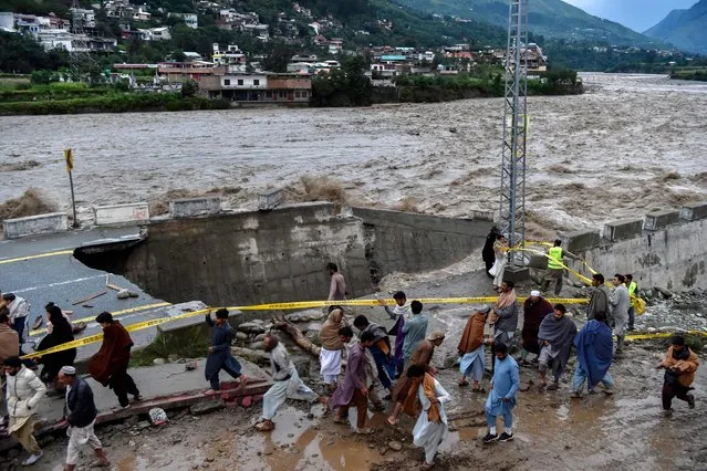People gather in front of a road damaged by flood waters following heavy monsoon rains in Madian area in Pakistan's northern Swat Valley on August 27, 2022. (Photo by Abdul Majeed/AFP Photo)
