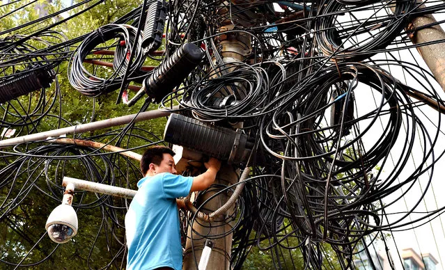 A worker makes repairs below electricity and communications cables on a pylon in Beijing on September 5, 2014. Shanghai stocks closed at a 17-month high on September 5 on hopes the Chinese government will introduce fresh measures to kickstart the world's number two economy. (Photo by Greg Baker/AFP Photo)