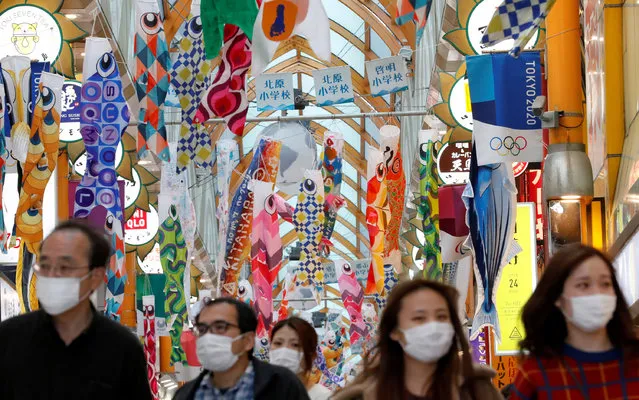 People wearing face masks walk under fluttering Koinobori, traditional Japanese carp-shaped windsocks that are hung in Japan from April to early May to wish a good health for children, following the coronavirus disease (COVID-19) outbreak, in Tokyo, Japan, April 24, 2020. (Photo by Kim Kyung-Hoon/Reuters)