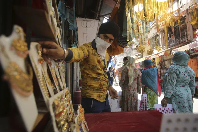 A shopkeeper displays jewelry for sale at a market area in Jammu, India, Wednesday, May 20, 2020. Small shops and other businesses were reopened in several states. E-commerce companies started to deliver goods, including those considered nonessential, to places outside containment zones. (Photo by Channi Anand/AP Photo)