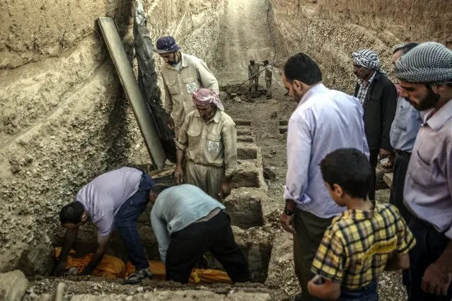 People observe as others lay down the body of a dead woman inside a grave in the multi-layered graveyard of Douma city, outskirts of Damascus, Syria, 18 August 2016. The Local Council of Douma started digging multi-layered graves as a solution for the massacre that happened in August of 2015 when more than 100 Syrian were killed in airstrikes on the Rebel-held city of Douma, 60 people were buried in two mass graves in that night. The graveyard always contains at least 40 empty graves in case of mass killing. The graves contains eight stairs, and is organized to bury the unknown on top in case they were identified later. (Photo by Mohammed Badra/EPA)