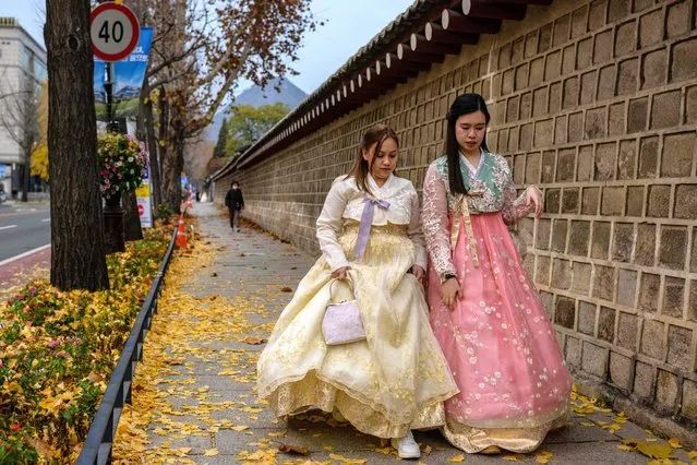 Women wear traditional Hanbok dresses as they walk past fallen autumn leaves in Seoul on November 21, 2022. (Photo by Anthony Wallace/AFP Photo)