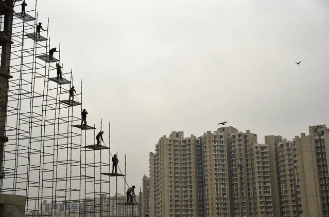Indian laborers standing on a scaffolding shift steel rods from the ground to the top of an under construction building in Greater Noida, India, Monday, February 12, 2018. (Photo by R.S. Iyer/AP Photo)