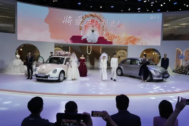 Visitors film models in wedding gowns showcasing the Ora, a Chinese-made electric car brand during the Auto Shanghai 2023 at the National Exhibition and Convention Center in Shanghai, China, Tuesday, April 18, 2023. (Photo by Ng Han Guan/AP Photo)