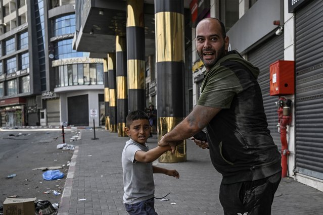 A man and young child react during clashes between Israeli soldiers and Palestinian gunmen in the centre of Jenin in the occupied West Bank on September 2, 2024. In Jenin, the streets were largely deserted and most shops were closed on September 2, after loud explosions and clashes were heard during the night while Israeli bulldozers caused damage to roads and infrastructure including water systems, according to Palestinian officials in the northern West Bank. (Photo by Ronaldo Schemidt/AFP Photo)