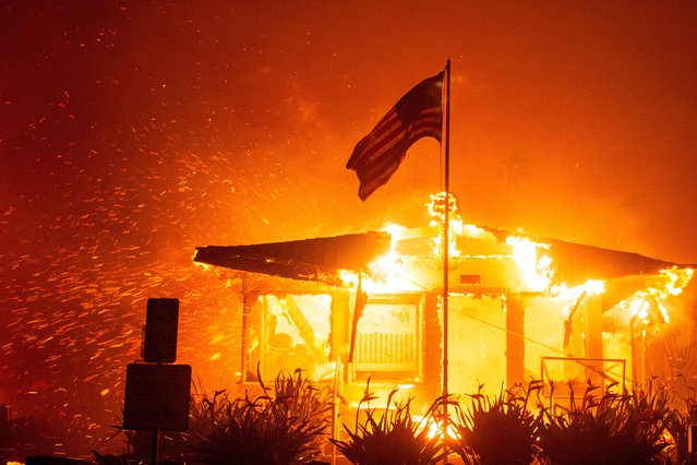 A U.S flag flies as fire engulfs a structure while the Palisades Fire burns during a windstorm on the west side of Los Angeles, California, U.S. January 7, 2025. (Photo by Ringo Chiu/Reuters)