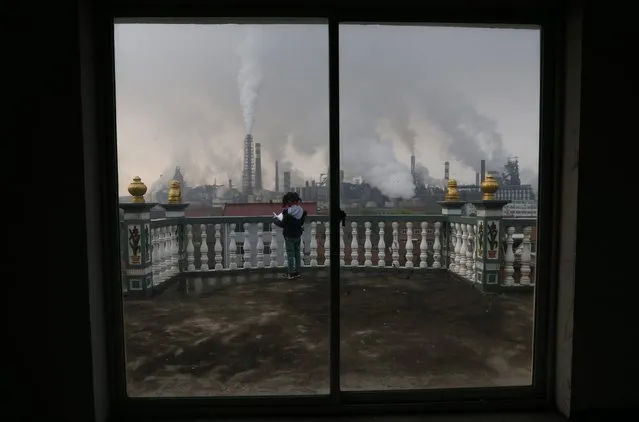 A girl reads a book on her balcony as smoke rises from chimneys of a steel plant, on a hazy day in Quzhou, Zhejiang province in this April 3, 2014 file photo. China's manufacturing growth stalled for the second straight month in January and companies had to cut prices at a faster clip to win new business, adding to worries about growing deflationary pressures in the economy, a private survey showed. (Photo by Reuters/Stringer)