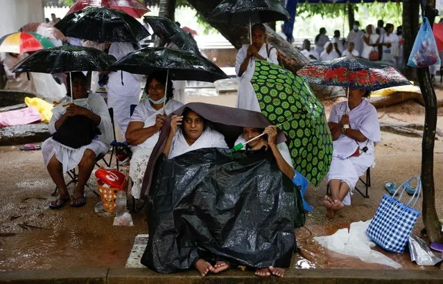Devotees hold up umbrellas and covers while they worship in heavy rain on Vesak day to commemorate the birth, enlightenment and death of Buddha, at Kelaniya Buddhist temple, in Colombo, Sri Lanka on May 5, 2023. (Photo by Dinuka Liyanawatte/Reuters)
