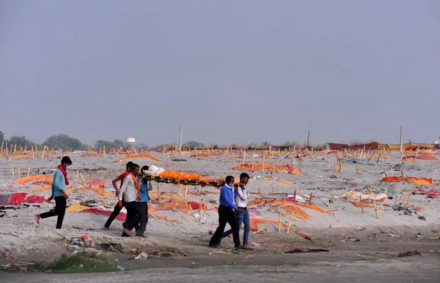 Relatives carry the body of a man for cremation after they, according to the relatives, were denied permission for his burial, past shallow sand graves of people, some of which are suspected to have died from the coronavirus disease (COVID-19), on the banks of the river Ganges in Shringaverpur on the outskirts of Prayagraj, India, May 21, 2021. (Photo by Ritesh Shukla/Reuters)