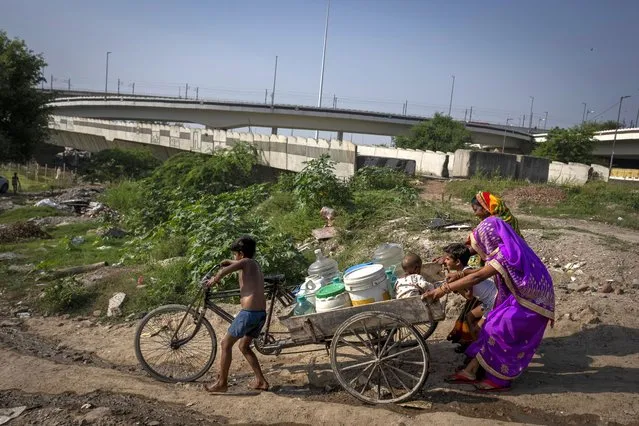 A young boy tries to steer his cycle carrier carrying drinking water down a steep slope as women try to control its speed on the way to flood plain of Yamuna River were they live in New Delhi, India, Friday, September 29, 2023. (Photo by Altaf Qadri/AP Photo)