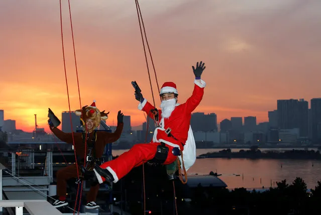 Window cleaners dressed as Santa Claus (R) and a reindeer pose for photographers as they clean a glass window at an event to celebrate the upcoming Christmas at DECKS Tokyo Beach in Tokyo, Japan, December 21, 2016. (Photo by Kim Kyung-Hoon/Reuters)