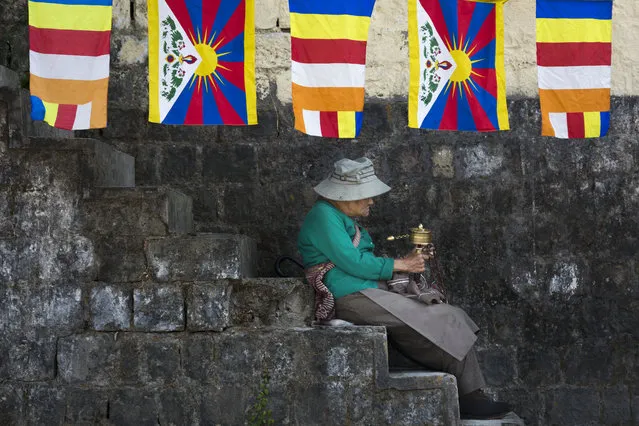 An exile Tibetan sits on the steps under a string of Tibetan and Buddhist flags as she waits to welcome her spiritual leader the Dalai Lama in Dharmsala, India, Sunday, November 25, 2018. The Tibetan leader returned Sunday after visiting Japan. (Photo by Ashwini Bhatia/AP Photo )