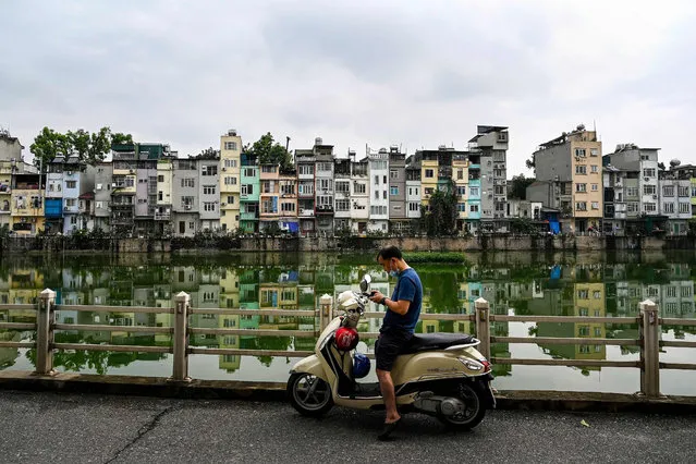 This photograph taken on June 8, 2021 shows a man checking his mobile phone against the bacdrop of narrow residential houses, known as “nha ong” in Vietnamese or “tube houses”, in an urban area of Hanoi. (Photo by Manan Vatsyayana/AFP Photo)