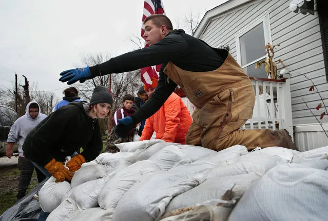 Sky Coleman, left, stacks a sandbag as Tyler Hopkins awaits another as a group of 15 middle and high school students from the nearby city of Louisiana, Mo., sandbagged the home of the aunt of a fellow student in Clarksville, Mo., Saturday, March 30, 2019. The Mississippi River reached 32.8 feet Saturday afternoon, entering major flood stage for the first time this spring. It is expected to crest late Sunday at 34.2 feet, more than three feet below the 37.7 foot record of 1993. (Photo by Robert Cohen/St. Louis Post-Dispatch via AP Photo)