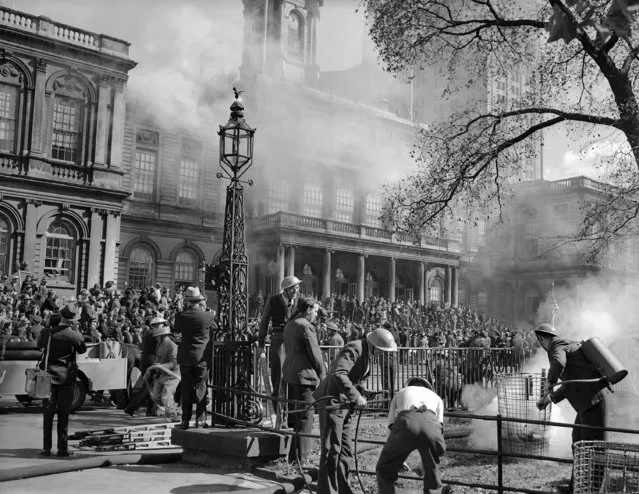 Fire Department auxiliary workers putting out a fire in City Hall Park in New York  October 11, 1941 while City Hall, in the background, smokes from fire bombs, during the Fire Defense Day demonstration which showed what could be done in case of an attack on New York City from the air. Regular firemen and civilian helpers, trained since July 11 in local firehouses, took part in the show. (Photo by Matty Zimmerman/AP Photo)