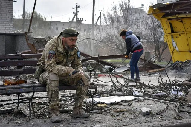 A Ukrainian serviceman smokes sitting on a bench as a local resident clears debris near a building damaged in the Russian air raid in the town of Orikhiv, Zaporizhzhia region, Ukraine, Friday, April  5, 2024. (Photo by Andriy Andriyenko/AP Photo)