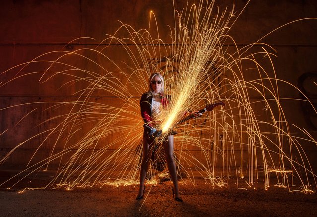 Event entertainer Holly Egan poses with a guitar using an angle grinder as Kevin Jay and Nigel Cox spin burning steel wool, sending sparks flying under the A13 in Essex, UK on April 4, 2024. (Photo by Kevin Jay/Picture Exclusive)