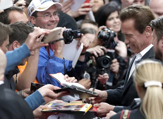 Actor Arnold Schwarzenegger, right, signs autographs as he arrives for the Europe premiere of his new movie 'Terminator: Genisys' in Berlin, Germany, Sunday, June 21, 2015. (AP Photo/Michael Sohn)