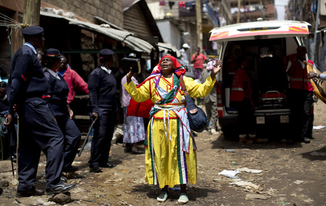 A follower of the Legio Maria church prays in the street next to a waiting ambulance, as rescuers nearby work to free a woman who had been trapped for six days in the rubble of a collapsed building, in the Huruma area of Nairobi, Kenya Thursday, May 5, 2016. (Photo by Ben Curtis/AP Photo)