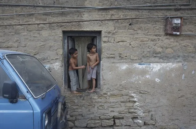 Siblings stand in the window of their single-room family quarters during a power outage in Karachi, Pakistan, July 8, 2015. (Photo by Akhtar Soomro/Reuters)