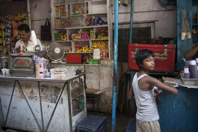 An Indian child reacts to the camera as he fills tea in plastic cup to be served to customers at a narrow alley in old quarters of Delhi, India, Saturday, July 25, 2015. India is the second largest tea producer in the world and the drink is the most popular hot beverage in the country. (Photo by Tsering Topgyal/AP Photo)