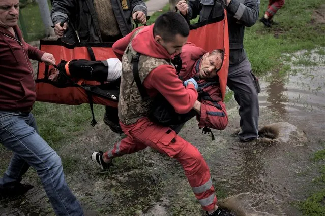 An emergency worker is helped by locals to carry a man to an ambulance following a Russian bombardment in Kharkiv, Ukraine, Wednesday, April 27, 2022. (Photo by Felipe Dana/AP Photo)