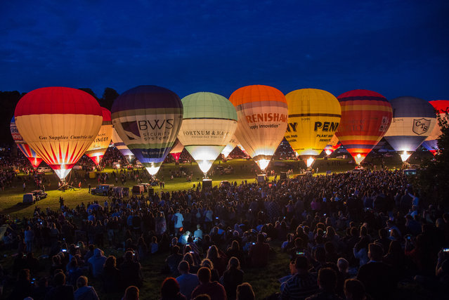 Crowds watch as tethered balloons are illuminated by their burners during the night glow evening event on the first day of the Bristol International Balloon Fiesta at the Ashton Court estate on August 6, 2015 in Bristol, England. Now in its 37th year, the Bristol International Balloon Fiesta is Europe's largest annual hot air balloon event in the city that is seen by many balloonists as the home of modern ballooning. (Photo by Matt Cardy/Getty Images)