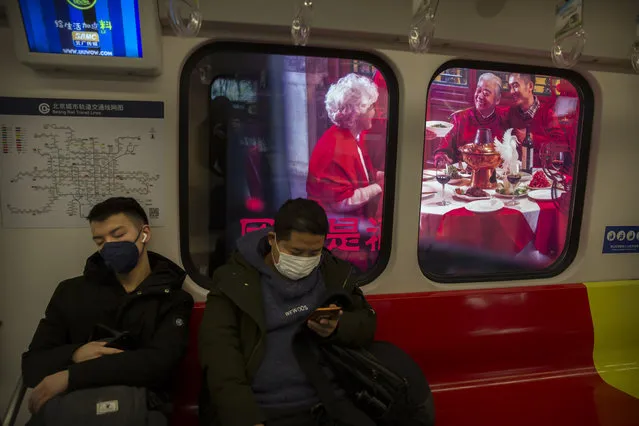 People wear masks on a subway train as it stops near a billboard showing a family having a New Year's banquet meal in Beijing, Friday, January 24, 2020. A virus that has killed more than two dozen people and sickened hundreds more has all but shut down China's biggest holiday of the year, the Lunar New Year. Instead of family reunions or sightseeing trips, many of the country's 1.4-billion people are hunkering down as the country scrambles to prevent the illness from spreading further. (Photo by Mark Schiefelbein/AP Photo)