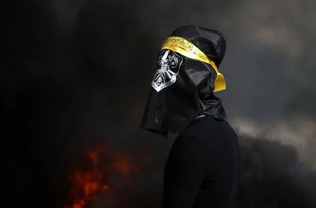 A Palestinian, his face covered by a flag, stands in front of buring tires during clashes with Israeli troops following a weekly demonstration against the expropriation of Palestinian land by Israel in the village of Kfar Qaddum near the Jewish settlement of Qadumim (Kedumim)(backgroubd), in the Israeli-occupied West Bank, on January 3, 2020. (Photo by Jaafar Ashtiyeh/AFP Photo)