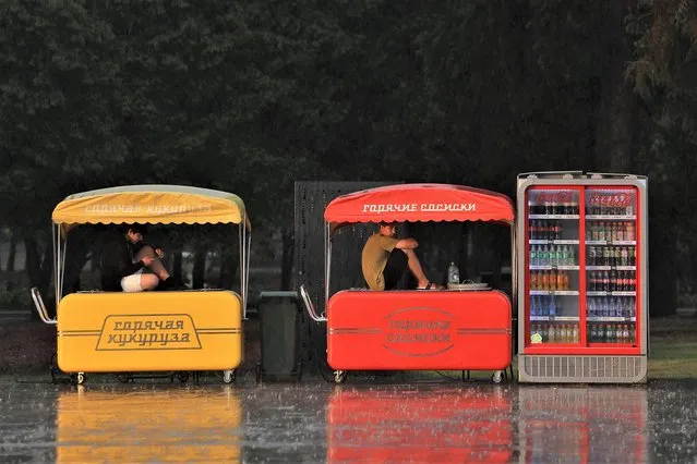 Vendors sit on kiosks as they take cover from heavy rain near the Northern River Station in Moscow, Russia on July 25, 2022. (Photo by Evgenia Novozhenina/Reuters)