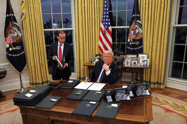 Donald Trump signs documents as he issues executive orders and pardons for January 6 defendants in the Oval Office on January 21, 2025. (Photo by Carlos Barria/Reuters)