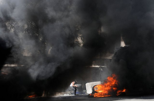 A Palestinian burns tyres at an Israeli army checkpoint during clashes, in Hebron in the Israeli-occupied West Bank on August 19, 2022. (Photo by Mussa Qawasma/Reuters)