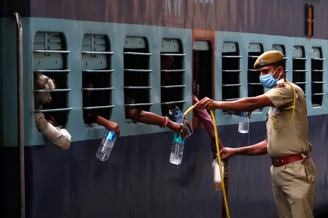 A policeman fills up bottles with drinking water to migrant workers of a special train service departing for Uttar Pradesh after a government eased a nationwide lockdown as a preventive measure against the COVID-19 coronavirus, in Ajmer on May 18, 2020. (Photo by Himanshu Sharma/AFP Photo)