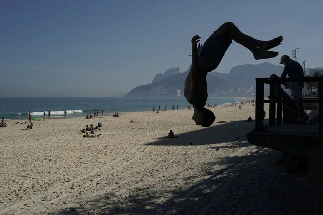 A young man somersaults on the Arpoador beach, amid the new coronavirus pandemic in Rio de Janeiro, Brazil, Saturday, June 20, 2020. Authorities have started to ease some restrictive measures in place to curb the spread of COVID-19, allowing individual water sports but sunbathing is still forbidden and people out in public are asked to wear protective face masks. (Photo by Leo Correa/AP Photo)