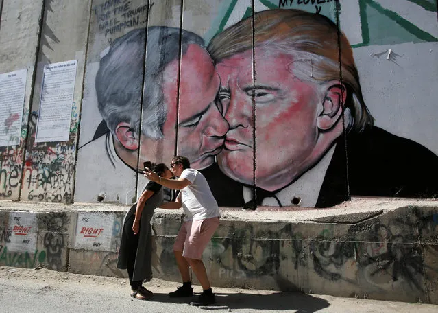Tourists kiss each other as they stand in front of a mural depicting U.S. President Donald Trump and Israel's Prime Minister Benjamin Netanyahu kisisng each other in the West Bank city of Bethlehem October 29, 2017. (Photo by Mussa Qawasma/Reuters)