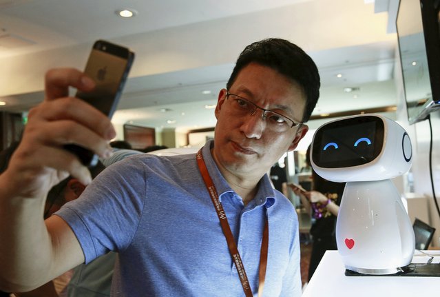 A visitor takes a selfie with Baidu's robot Xiaodu at the 2015 Baidu World Conference in Beijing, China, September 8, 2015. Xiaodu, an artificial intelligent robot developed by Baidu, has access to the company's search engine database and can respond to voice commands, Baidu says. (Photo by Kim Kyung-Hoon/Reuters)