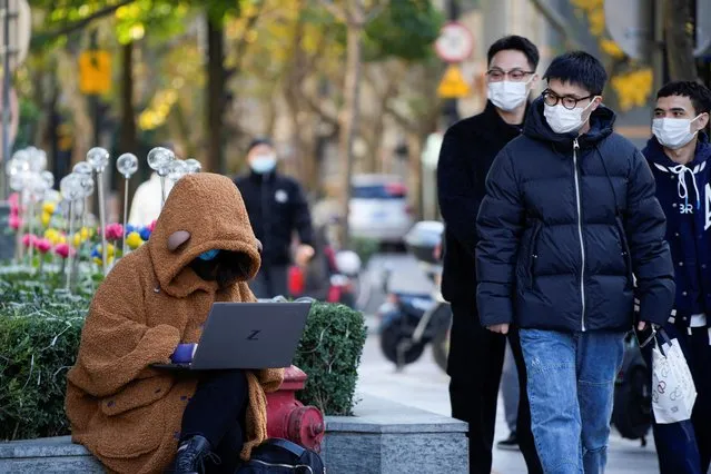 A woman wearing a face mask looks at her laptop on a street, as coronavirus disease (COVID-19) outbreaks continue in Shanghai, China on December 14, 2022. (Photo by Aly Song/Reuters)